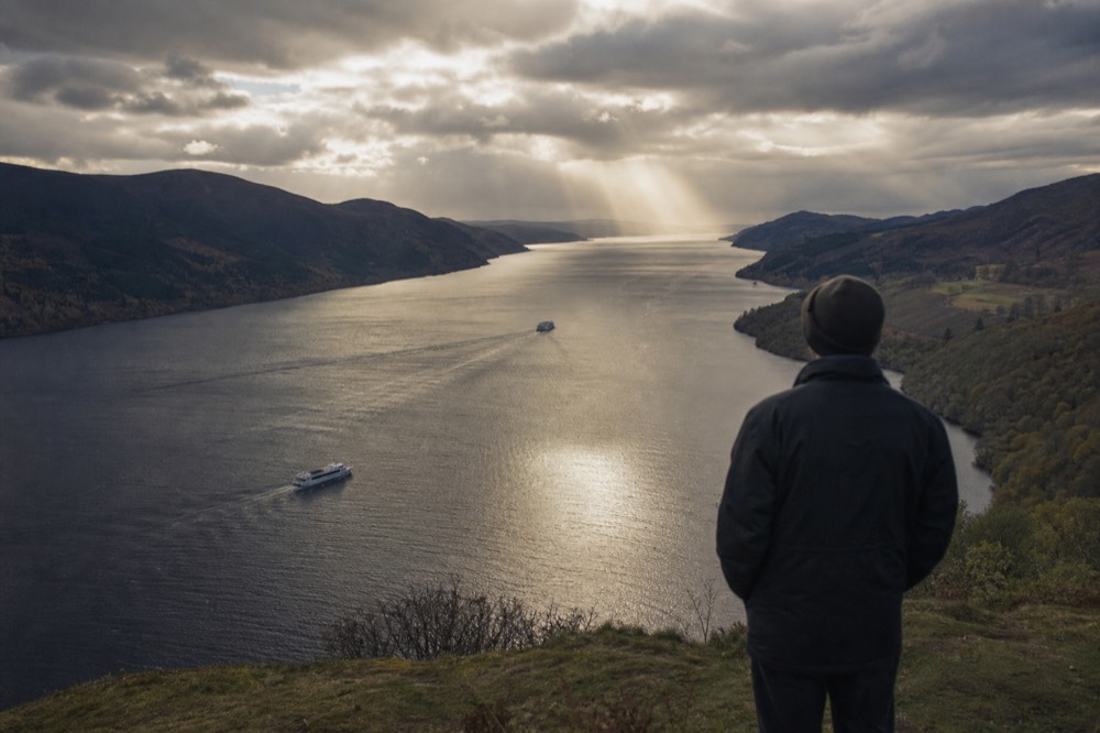 The long view down Loch Ness from a shingle beach, dark water stretching between steep Highland hills