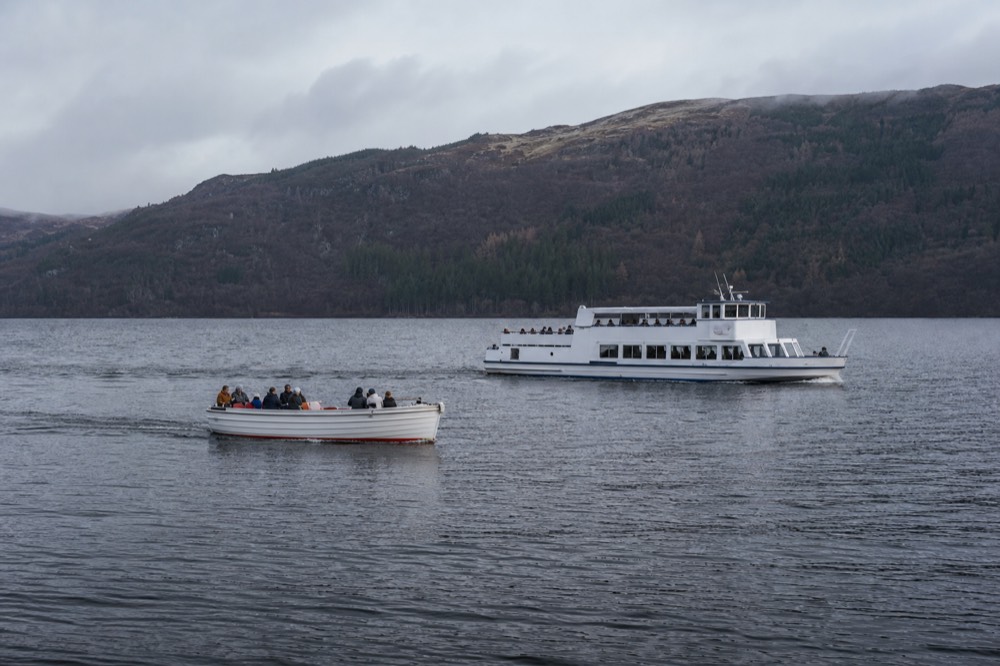 A cruise boat under way on Loch Ness in low golden evening light, warm colour on the ridges behind